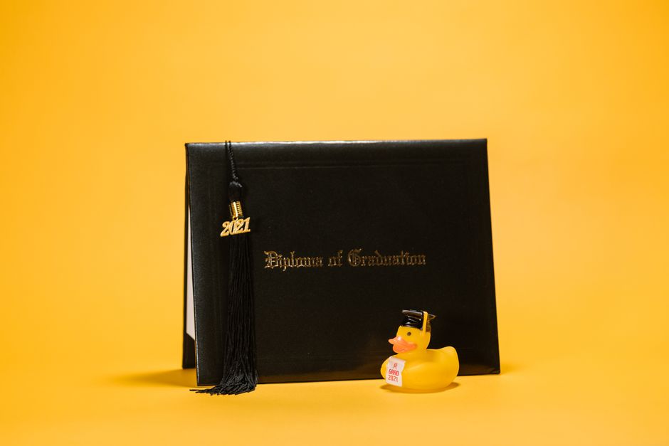 Close-up of a diploma with tassel and a rubber duck on a yellow background.