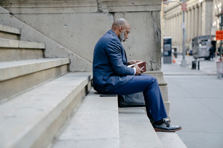 A professional man sits on urban steps holding a notebook, captured in an outdoor city setting.