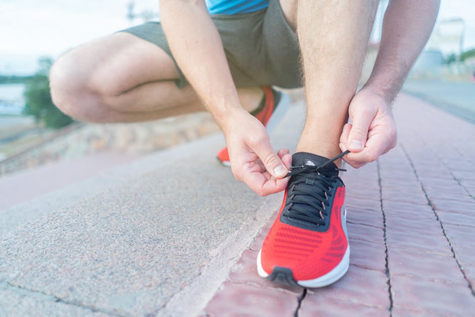 Close-up of an adult tying red sneakers on a sunny outdoor pathway.