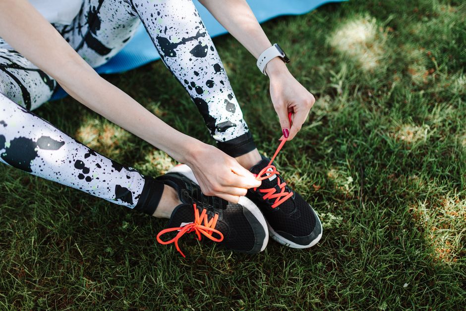 Close-up of a woman tying bright shoelaces on sneakers outdoors, preparing for exercise.