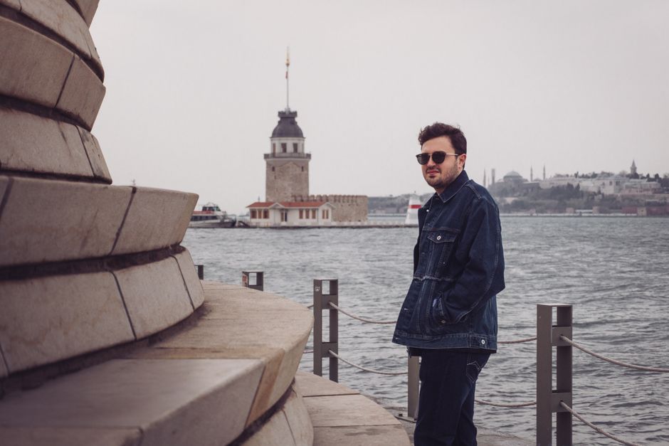 A man stands by the Bosphorus with İstanbul's iconic Maiden's Tower in the background, embodying city life.