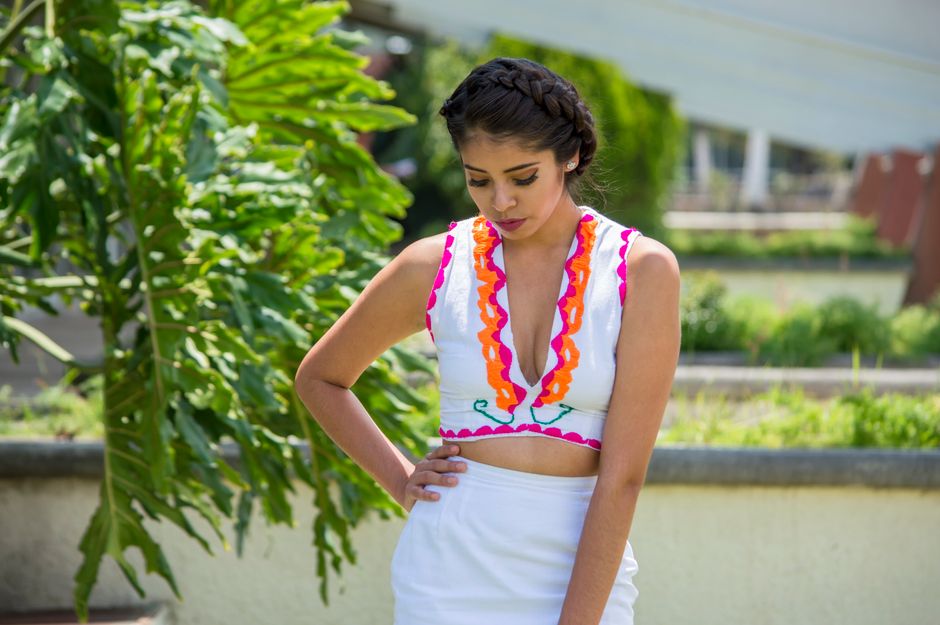 A woman in a vibrant traditional dress poses outdoors in natural daylight.