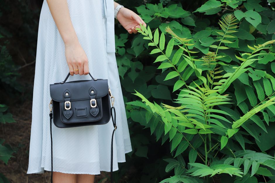 Close-up of a woman holding a black handbag, wearing a striped dress, beside lush green pl