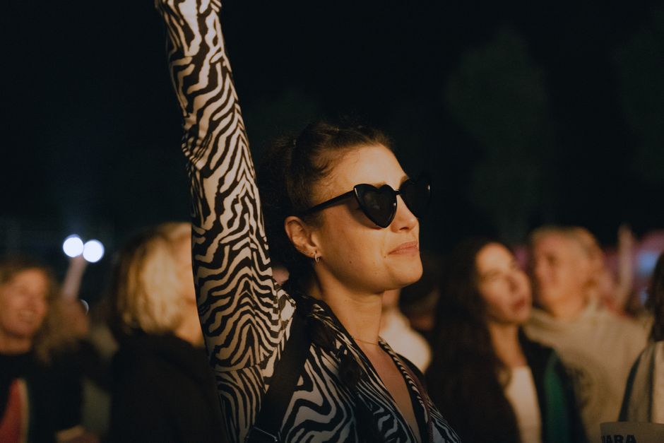A woman in sunglasses raises her arm at an outdoor concert at night.