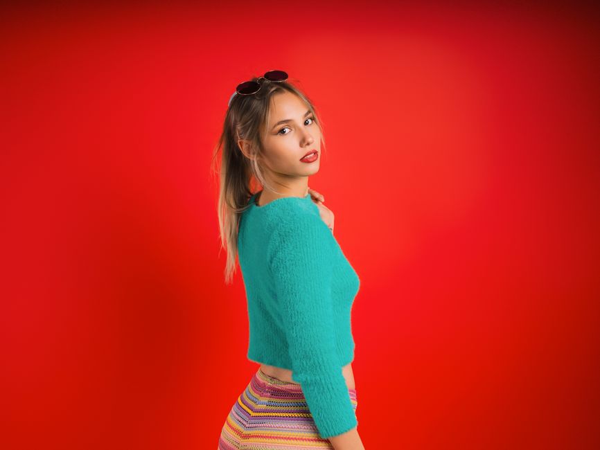 Stylish young woman posing against a vivid red background, wearing colorful attire and sunglasses.