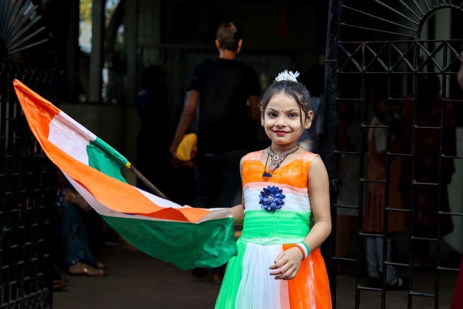 Smiling girl in tricolor dress holds Indian flag during Independence Day celebration in India.
