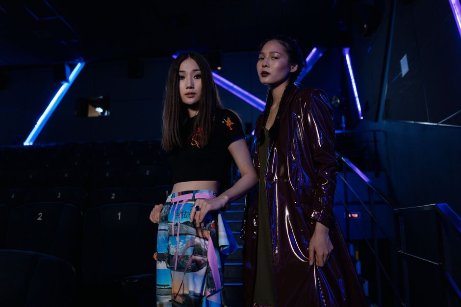 Stylish Asian women posing confidently in a modern cinema environment with vibrant lighting.