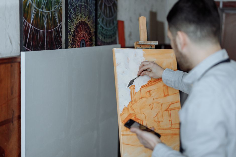 Artist working on canvas in studio, creating abstract art with paint and brushes.