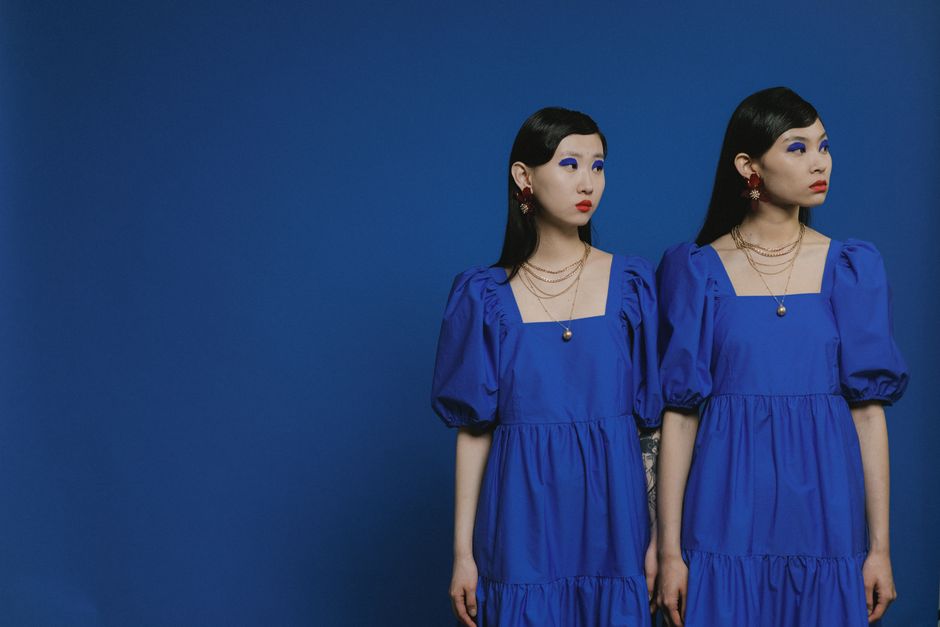 Stylish portrait of two women in matching blue dresses with bold makeup.