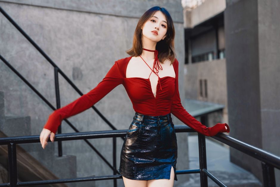 Young woman posing outdoors in fashionable red top and black leather skirt, capturing modern style.