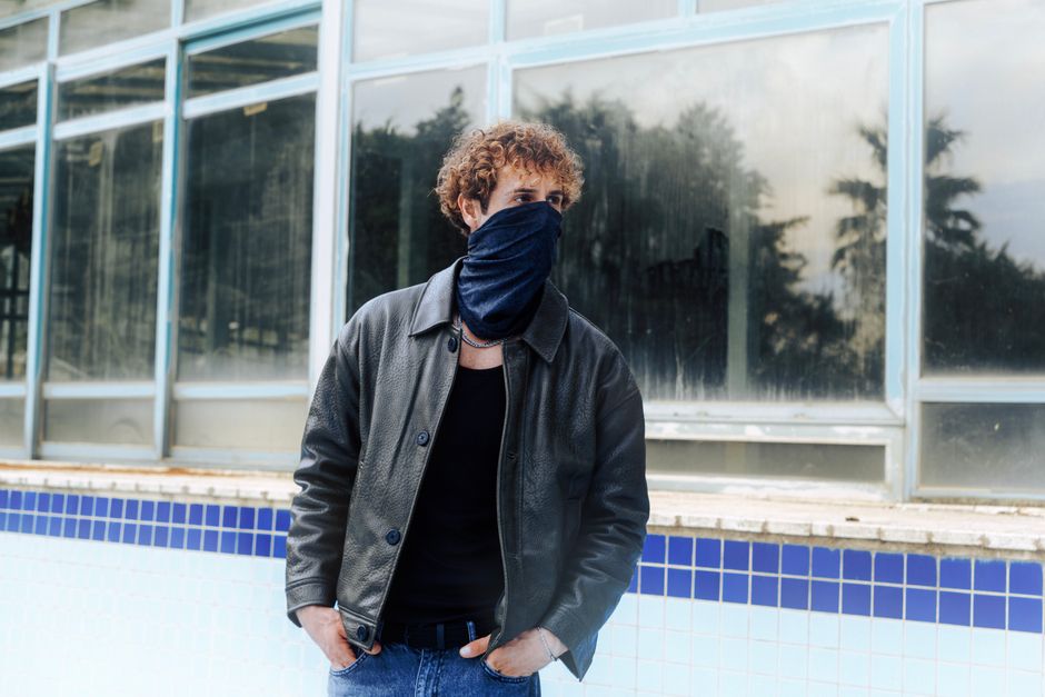 A man with a covered face stands by an abandoned building, evoking mystery and intrigue.