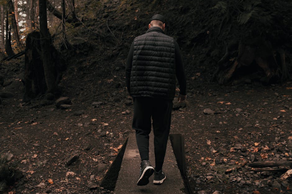 An adventurer in a puffer jacket walks through a shadowy forest trail.