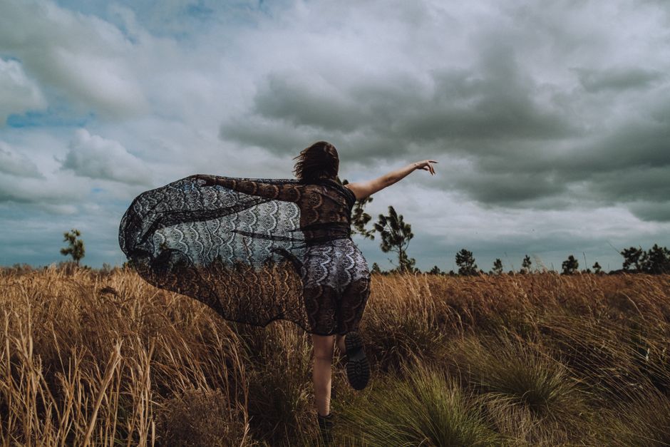 A woman dances with grace in a field under a cloudy sky, draped in a laced sarong.