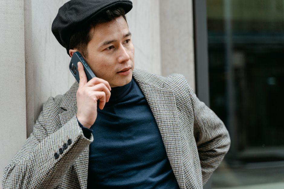 A fashionable man wearing a beret and blazer makes a phone call, conveying modern style.