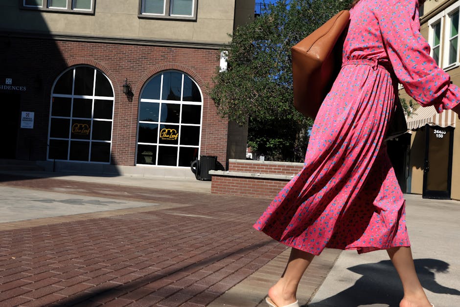 A woman in a pink floral dress walking, capturing fashion and movement in a sunny urban environment.