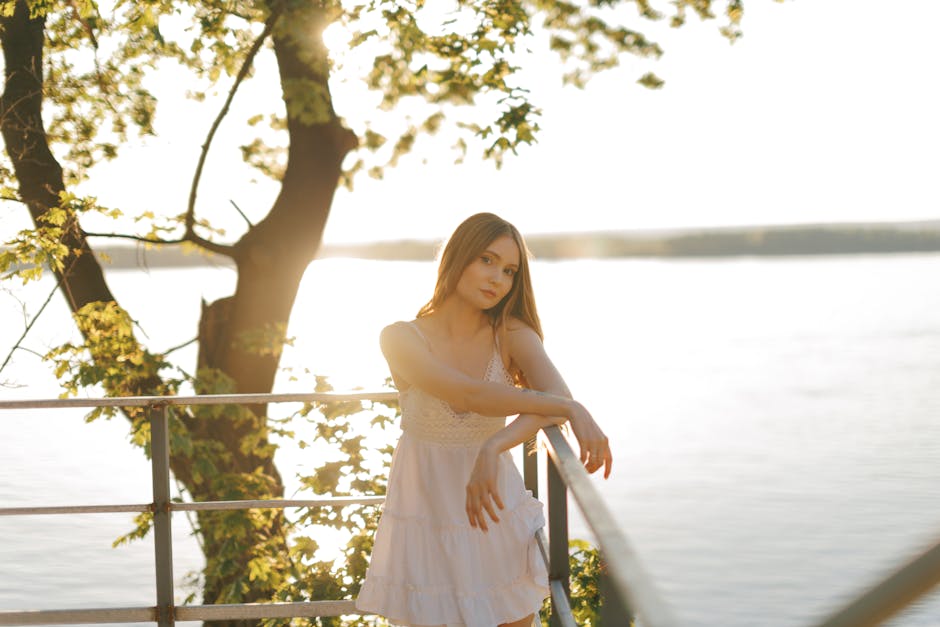 Serene portrait of a young woman in a white dress by the lake during sunset.