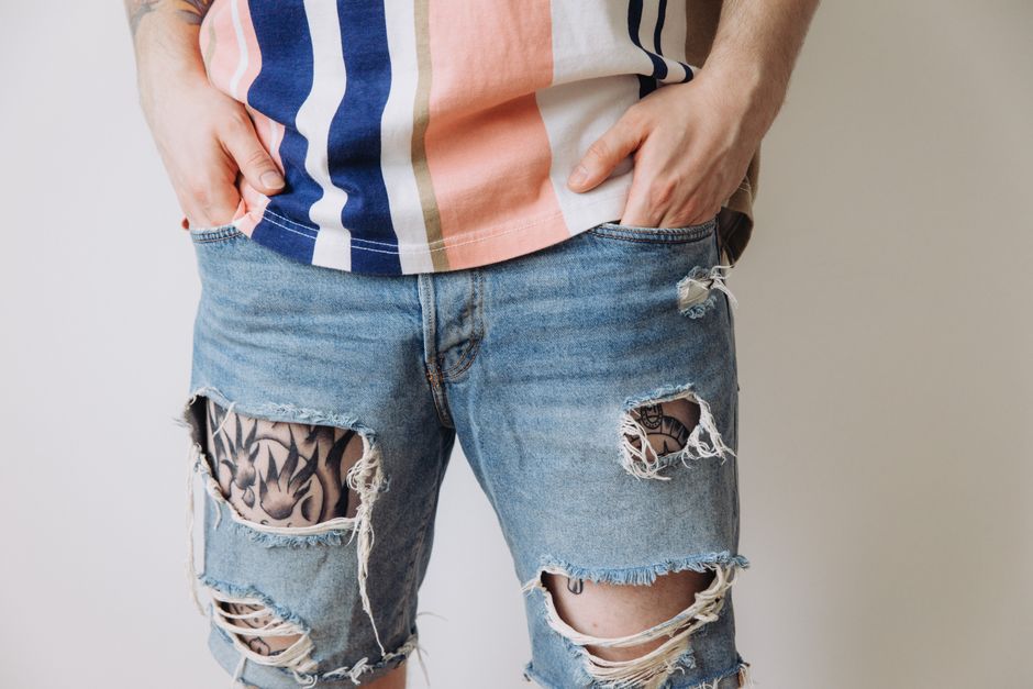 Close-up of a person in ripped denim shorts and a striped shirt with tattoos visible.