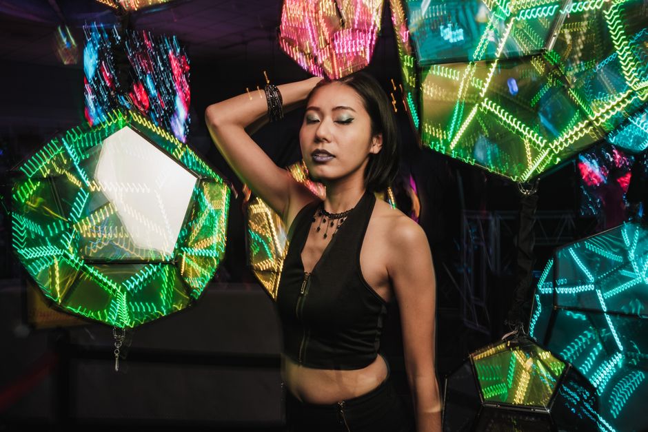 Stylish woman poses with eyes closed amidst colorful neon geometric lights.