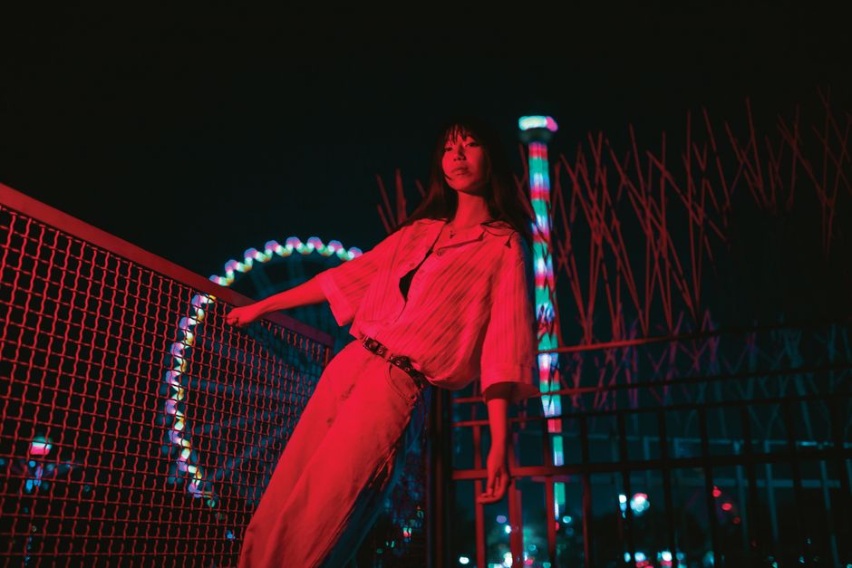 Woman in red light at night by a Ferris wheel, creating a vibrant city vibe.