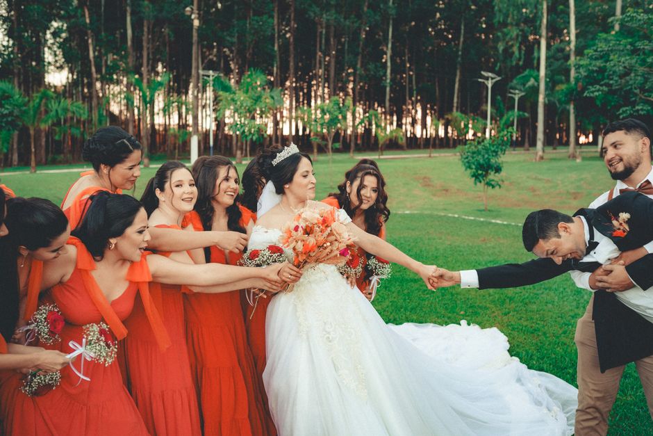 A lively outdoor wedding with bridesmaids pulling the bride, creating joy and laughter.