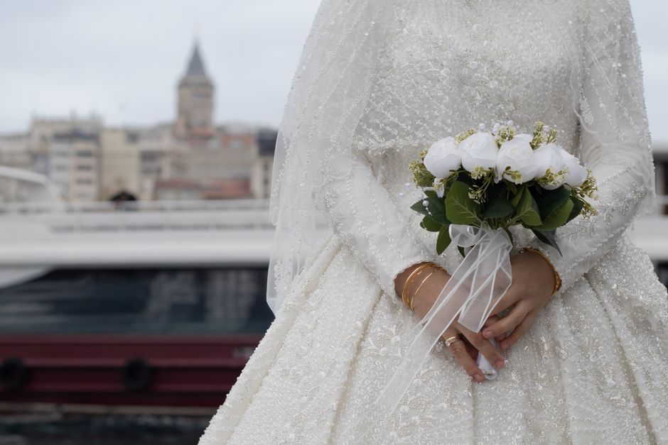 Bride in elegant dress holding bouquet against cityscape background, showcasing romantic elegance.