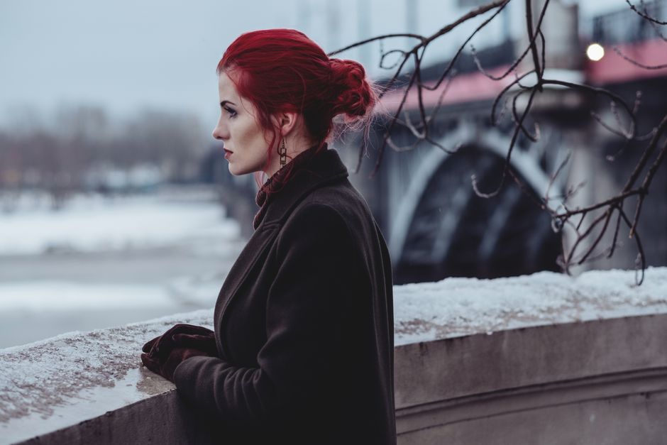 A woman with red hair gazes into the distance on a snowy winter day.