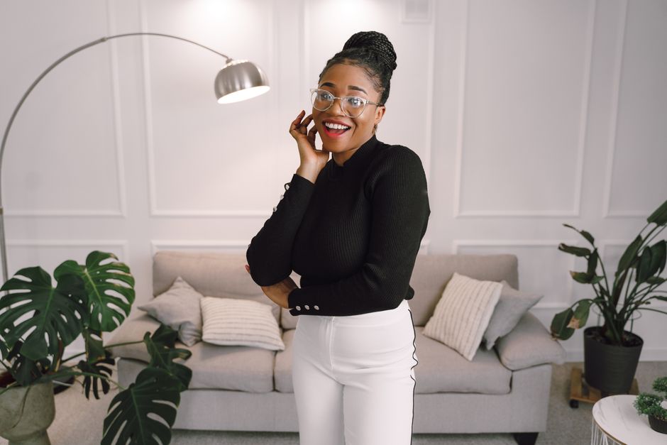 A smiling woman with eyeglasses poses in a modern living room with potted plants.