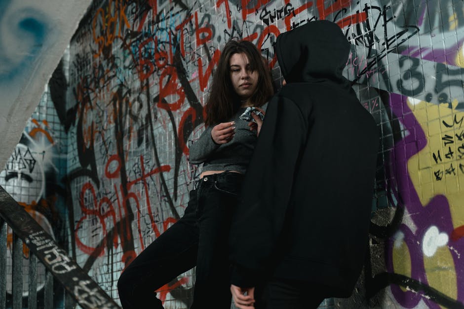 Two young individuals in hoodies stand against a graffiti-covered wall, embodying urban street style.